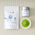Tezumi Classics Umezuki matcha pouch with a plum branch and blue moon design beside a silver tin and a dish of matcha powder.