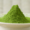 Deep green Umezuki matcha powder heaped in a tall cone in a pale ceramic bowl, side view.