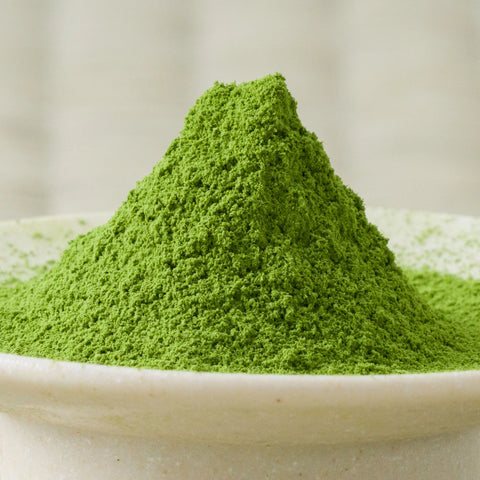 Deep green Umezuki matcha powder heaped in a tall cone in a pale ceramic bowl, side view.