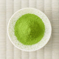 Green Umezuki matcha powder mounded in a white dish, viewed from above on a tatami mat.