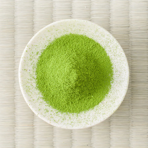 Green Umezuki matcha powder mounded in a white dish, viewed from above on a tatami mat.