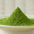 Deep green Wakatake matcha powder heaped in a cone in a pale ceramic bowl, side view.