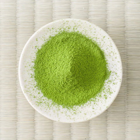 Green Wakatake matcha powder mounded in a white dish on a tatami mat, overhead view.