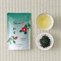 Teal Wakō Sencha pouch printed 和香 with a red camellia, on tatami beside a cup of brewed tea and a dish of leaf