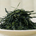 Macro view of hand-picked Wakō sencha, unusually long dark green needles mounded in a pale ceramic bowl