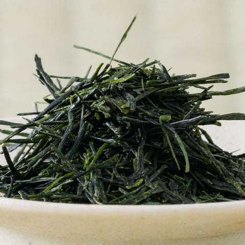 Macro view of hand-picked Wakō sencha, unusually long dark green needles mounded in a pale ceramic bowl