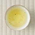Wakō sencha brewed to a pale greenish-yellow liquor in a speckled white cup, viewed from overhead