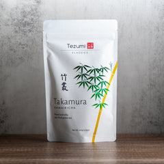 Tezumi Classics Takamura Kamairicha tea package on a wooden surface with a gray background