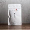 Tezumi Specialty Uji Okumidori Sencha package on a wooden surface with a gray background