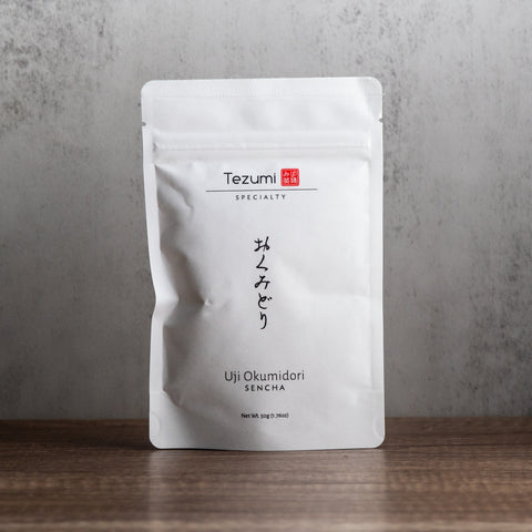Tezumi Specialty Uji Okumidori Sencha package on a wooden surface with a gray background
