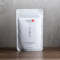 Tezumi Sencha tea package on a wooden surface with a gray background