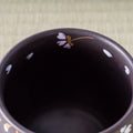 Close-up of a dark ceramic cup with floral designs on a textured surface