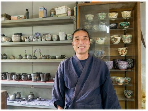 Murakami-san standing in front of a display of ceramic items in his store.