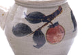 Close-up of the painted red fruit and blue foliage motif on the cream-grey body.