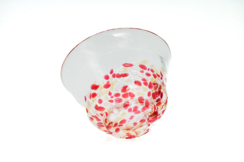 Clear glass teacup with pink, red, and yellow speckles on a white background