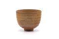 Amber-brown matcha chawan with a faint incised scene, shown from a three-quarter front angle.