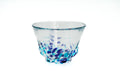 Clear glass teacup with light and dark blue speckles on a white background
