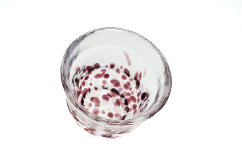 Clear glass teacup with purple and white speckles on a white background