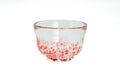 Clear glass matcha bowl with pink and red specks on a white background