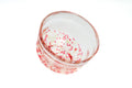 Clear glass matcha bowl with pink and red specks on a white background