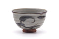 Grey Karatsu-yaki chawan with dark brushwork and a red-clay foot, shown from a three-quarter angle.