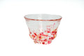 Clear glass teacup with pink, red, and yellow speckles on a white background