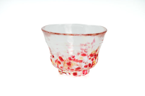 Clear glass teacup with pink, red, and yellow speckles on a white background