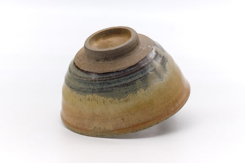 The chawan tilted to a three-quarter overhead angle, showing the exposed clay foot and banded glaze on the underside.