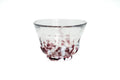 Clear glass teacup with purple and white speckles on a white background
