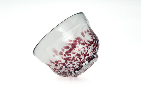 Clear glass matcha bowl with purple specks on a white background