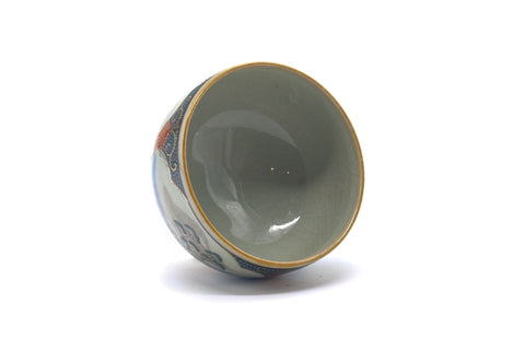 The cup tilted to show the pale glazed interior and gilt rim.