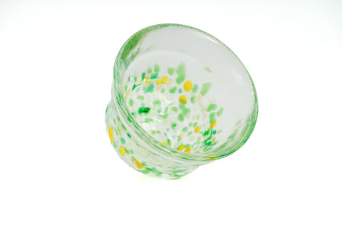 Clear glass teacup with green and yellow speckles on a white background
