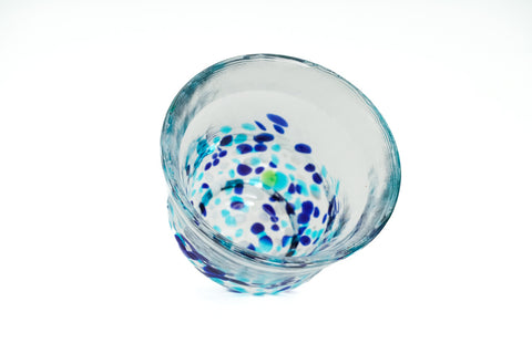 Clear glass teacup with light and dark blue speckles on a white background