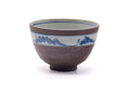Brown-purple matcha bowl (chawan) with a blue painted band of stylised mountains around the rim, three-quarter view