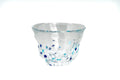 Clear glass teacup with white and blue speckles on a white background
