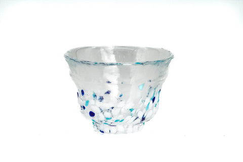 Clear glass teacup with white and blue speckles on a white background