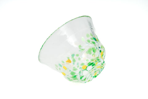 Clear glass teacup with green and yellow speckles on a white background
