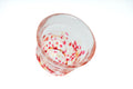 Clear glass teacup with pink, red, and yellow speckles on a white background