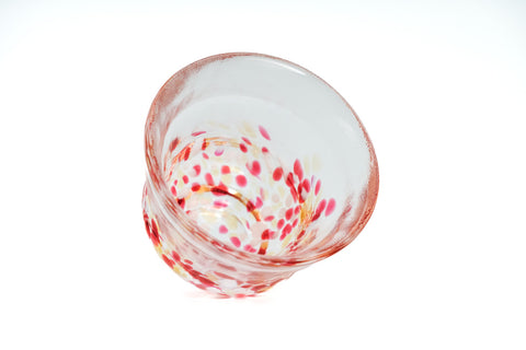 Clear glass teacup with pink, red, and yellow speckles on a white background