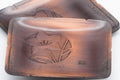 Closeup of a copper plate showing the embossed flower, indented edge, and maker's mark.