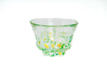 Clear glass teacup with green and yellow speckles on a white background