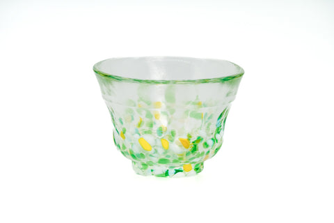 Clear glass teacup with green and yellow speckles on a white background