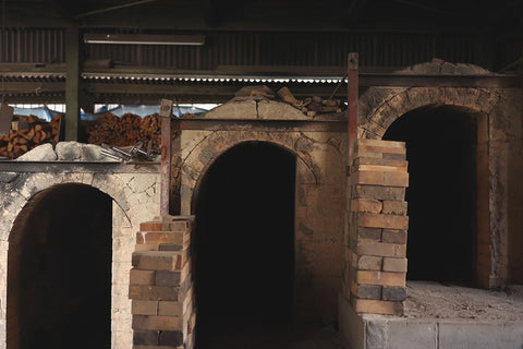 Twin brick kiln chambers of the Genso kiln, arched mouths bricked up and firewood stacked alongside