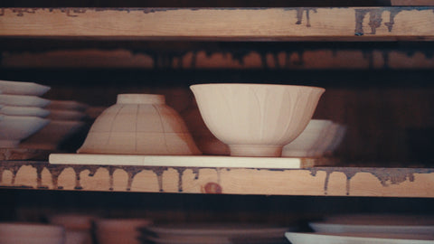 A single unglazed bowl resting on a glaze-spattered wooden kiln shelf