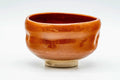 Three-quarter view of the glossy orange-red aka-raku chawan