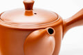 Three-quarter view of the red shudei Tokoname kyusu with lid on, showing the glossy orange clay