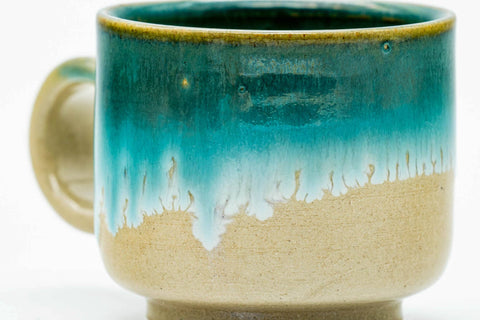 Close-up of a single cup, showing the turquoise glaze dripping over the beige body.