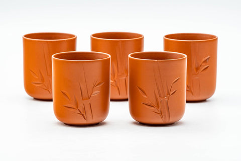 The five red yunomi cups arranged in a row, with engraved bamboo detailing.