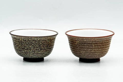 The matching pair of yunomi side by side, front view, showing their speckled brown surface and white floral sprigs