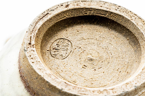 Underside of a cup showing the unglazed foot ring and an impressed maker's stamp.